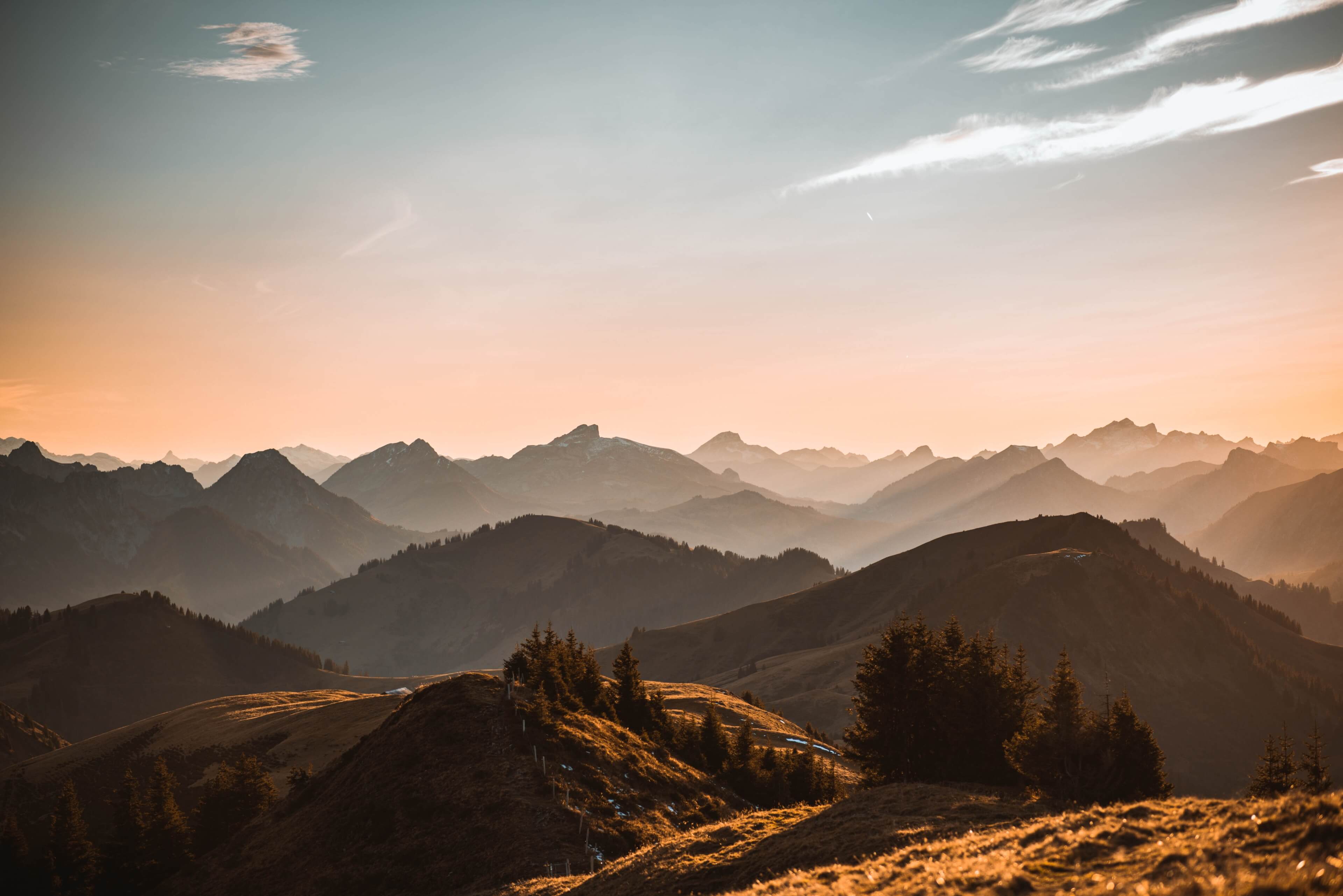 A serene landscape of layered mountain ridges fading into the distance, bathed in soft pastel hues of blue and peach under a calm sky.